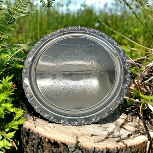 May include: A silver serving tray with a decorative grapevine design. The tray has a scalloped edge and is made of polished metal.