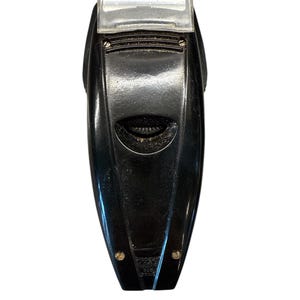 Puede incluir: Una afeitadora el&eacute;ctrica negra vintage con una cubierta protectora de pl&aacute;stico transparente. La afeitadora tiene un dise&ntilde;o aerodin&aacute;mico con un agarre texturizado y dos peque&ntilde;os detalles dorados en la parte inferior.