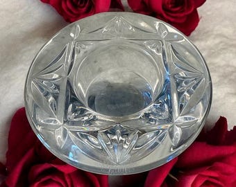 May include: A clear, round crystal candle holder with a geometric design. The candle holder is surrounded by several red roses. The text "Waterford" is visible on the side of the candle holder.