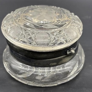 May include: A vintage glass and silver trinket box with a detailed etched design. The lid is clear glass with a silver rim and the base is clear glass with a silver band.