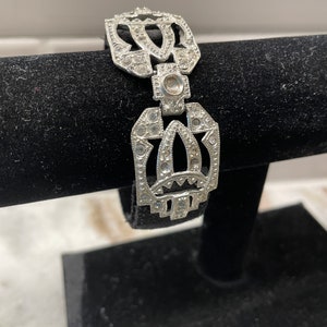 May include: A silver bracelet with a geometric design and clear rhinestones. The bracelet is on a black velvet display stand.