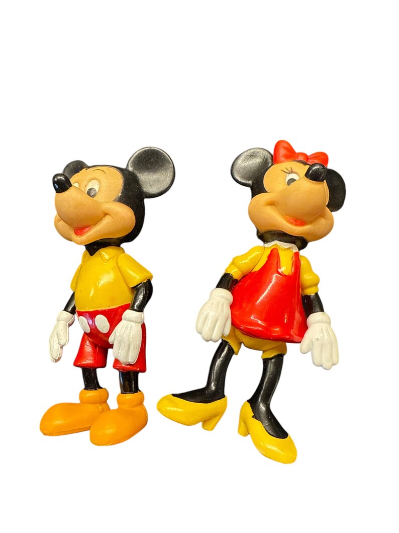 Pode incluir: Duas figuras vintage do Mickey Mouse e da Minnie Mouse. Mickey usa uma camisa amarela, cal&ccedil;&otilde;es vermelhos e sapatos laranja. Minnie usa um vestido vermelho, sapatos amarelos e um la&ccedil;o vermelho. Ambos t&ecirc;m luvas brancas e orelhas pretas.
