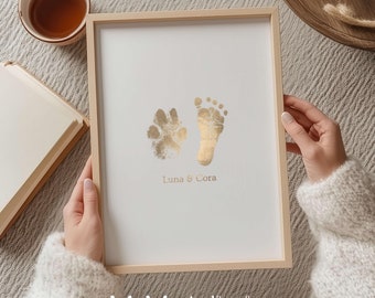 May include: A framed print with gold foil paw print and footprint, with the names Luna & Cora written below. The print is in a light wood frame and is being held by a person's hands.