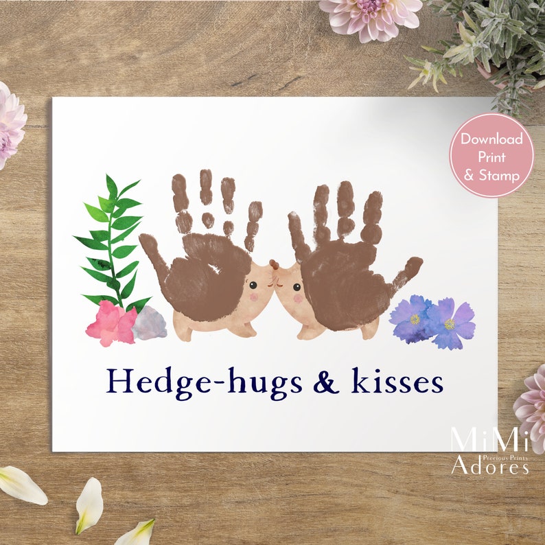 Op de afbeelding: Printbare kunst met twee bruine egels gemaakt met handafdrukken, omringd door groene bladeren, roze bloemen en paarse bloemen. De tekst "Hedge-hugs & kisses" staat in blauw onder de egels.