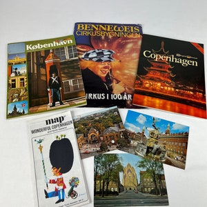 May include: A collection of vintage postcards and brochures featuring images of Copenhagen, Denmark. The postcards show various landmarks, including a church, a fountain, and a building with a clock tower. The brochures feature images of a clown, a guard, and a map of the city.