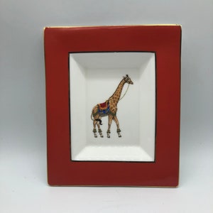 Könnte beinhalten: Ein rotes Porzellanserviertablett mit goldener Einfassung hat einen weißen Innenraum mit einem handgemalten Bild einer Giraffe, die einen Sattel trägt.