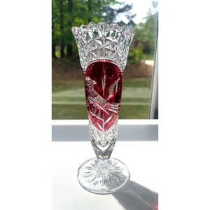 May include: A clear crystal vase with a ruby red centre section featuring a detailed bird and leaf design. The vase has a flared top and a round base, showcasing intricate cut patterns. The vase is approximately 25 cm tall.