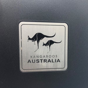 May include: A silver metal sign with two black kangaroos, one larger than the other, and the text "Kangaroos Australia".