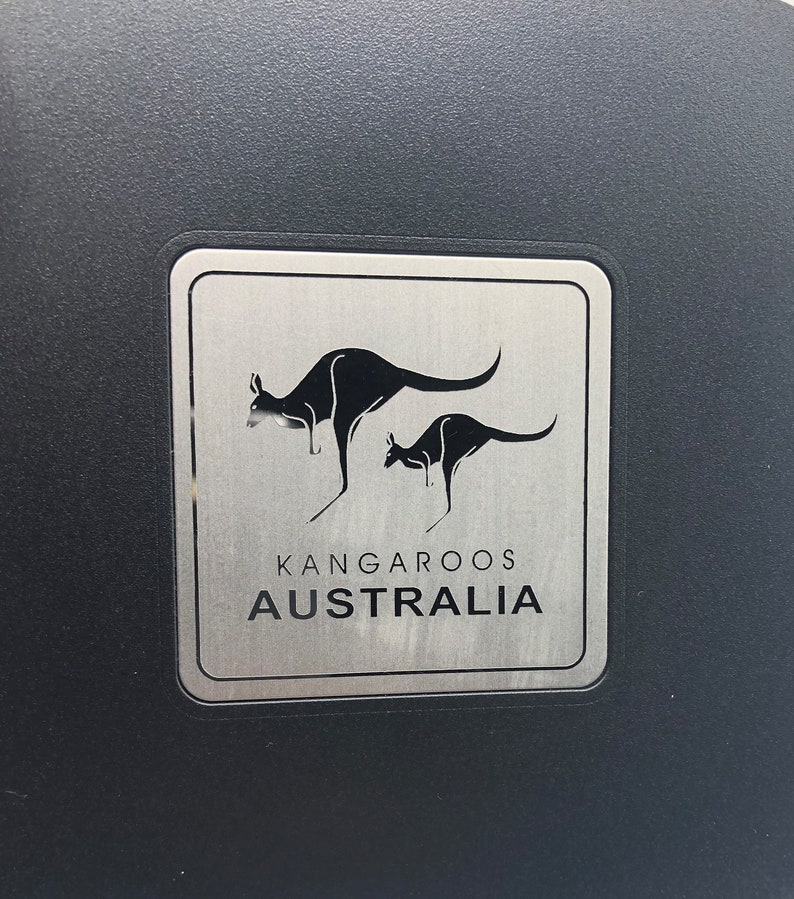 May include: A silver metal sign with two black kangaroos, one larger than the other, and the text "Kangaroos Australia".