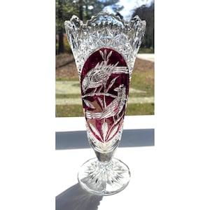 May include: A clear crystal vase with a ruby red oval panel featuring etched birds on branches. The vase has a starburst base and a scalloped rim. The vase is approximately 10 inches tall.