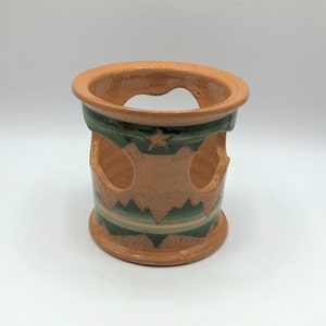 May include: A terracotta ceramic candle holder with green and white geometric designs. The holder has three open spaces for candles.