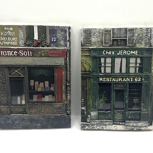 May include: Two vintage-style Parisian storefront scenes. The left storefront is a newsstand with the text "France-Soir" and "LIBRAIRIE PAPETE". The right storefront is a restaurant called "Chez JEROME" with the text "RESTAURANT 62".