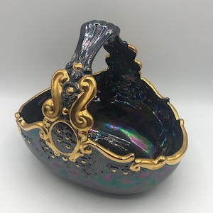 May include: A black and gold ceramic basket with an iridescent finish and ornate detailing. The basket has a handle and is shaped like a half-circle.