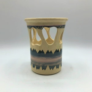 May include: A ceramic vase with a cream-colored base and a geometric pattern in black and pink. The vase has cutouts around the middle.