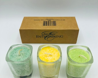 Op de afbeelding: Set van drie glazen kaarsenpotten met groene, gele en witte kaarsen. De kaarsen zijn gelabeld met "Taste of Home ENTERTAINING".