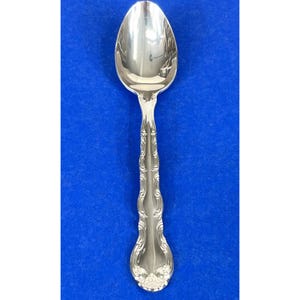 Puede incluir: Una cucharadita de plata con un mango adornado y detallado. La cuchara tiene un cuenco redondeado y un acabado pulido.