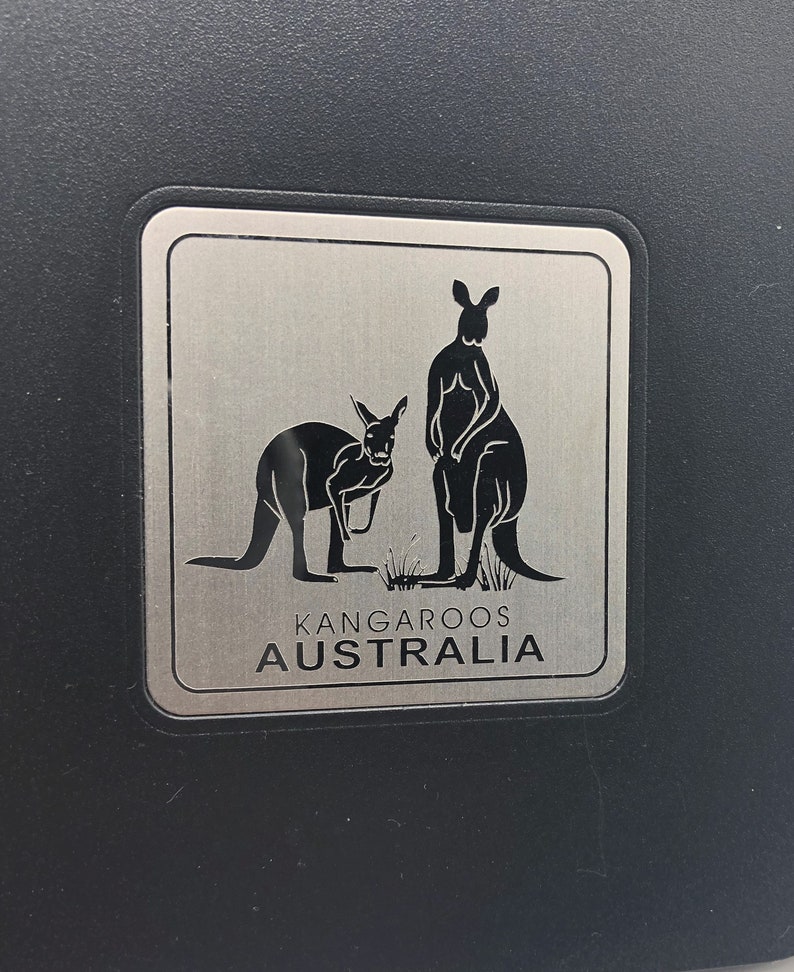 May include: A silver metal sign with two black silhouettes of kangaroos. The sign reads "Kangaroos Australia".