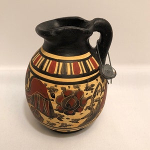 May include: Black and white ceramic pitcher with red and gold painted designs. The pitcher has a round body and a small handle. The design features a stylized bird and floral motifs.