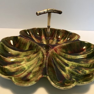 May include: A green and red clover-shaped ceramic serving dish with a metal handle. The dish has four sections and is perfect for serving snacks or appetizers.