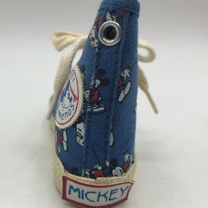 May include: Blue canvas high-top sneaker with a Mickey Mouse print. The shoe has a white lace and a white sole with the word "MICKEY" printed on it. The shoe also has a small circular patch with the words "Mickey's Friends" printed on it.
