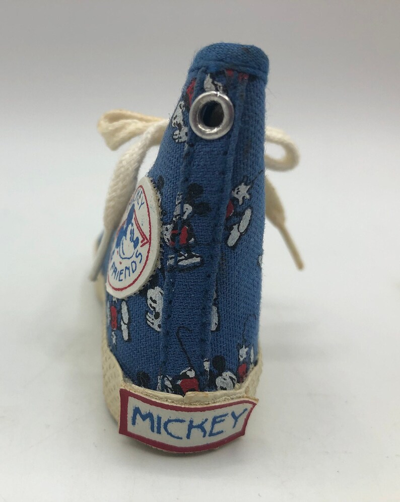 May include: Blue canvas high-top sneaker with a Mickey Mouse print. The shoe has a white lace and a white sole with the word "MICKEY" printed on it. The shoe also has a small circular patch with the words "Mickey's Friends" printed on it.
