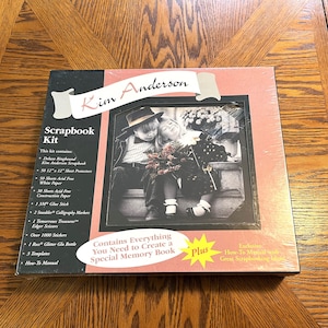 Può includere: Un kit per album di ritagli con una copertina rosa e nera che presenta una foto in bianco e nero di due bambini. Il kit include tutto ciò di cui hai bisogno per creare un album di ricordi speciale, tra cui carta senza acidi, colla, pennarelli e molto altro. Il kit include anche un manuale di istruzioni esclusivo con fantastiche idee per album di ritagli.