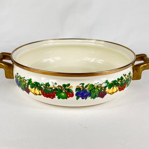 Può includere: Tegame in smalto bianco con manici dorati e un motivo di frutta colorata attorno al bordo.