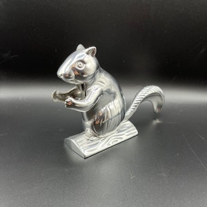 May include: A silver squirrel nutcracker with a detailed design. The squirrel is holding a nut in its paws and has a tail that acts as a lever.