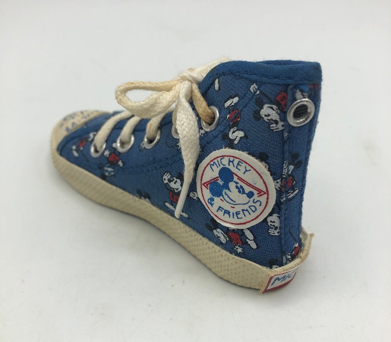 May include: Blue canvas high-top trainers with a white lace-up fastening. The trainers feature a Mickey Mouse and Friends print and a red, white and blue logo that says "Mickey & Friends".