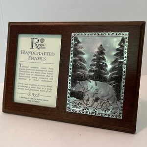 May include: A brown wooden picture frame with a silver metal inlay depicting a bear in a forest. The frame has a label that reads "Regal Art & Gifts" and "Handcrafted Frames". The label also includes the text "3.5x5" and "Made in Thailand".