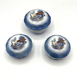 May include: Three small, round, blue and white ceramic trinket boxes with a floral design and a small house in the center.
