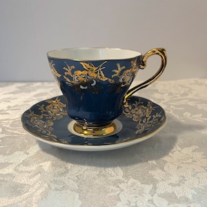 May include: A blue and gold teacup and saucer set with a floral pattern. The cup and saucer are both decorated with gold trim and a floral design.