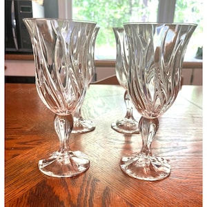 May include: Set of four clear glass wine glasses with a swirling, textured design. The glasses have a tall, slender stem and a wide bowl.