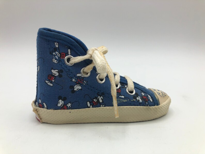 May include: Blue canvas high-top trainers with a white sole and white laces. The trainers are covered in a pattern of Mickey Mouse characters.