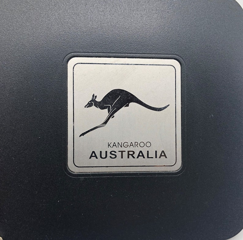 May include: A silver metal plaque with a black silhouette of a kangaroo jumping. The plaque has the words "Kangaroo Australia" printed on it.