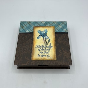 May include: A brown wooden box with a blue and brown plaid pattern on the top. The front of the box features a vintage-style image of a blue iris flower with a gold frame. The image also includes the text "May the beauty of the Lord our God be upon us. Psalm 90:17."
