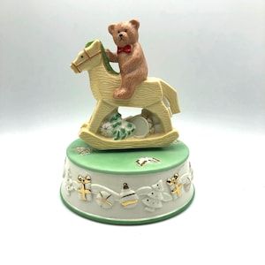 Mikasa Porcelain Musical Teddy Bear on a Rocking Horse with Toys and Gifts.  Rotates as the melody Noel plays.  On/off knob on bottom.  NIB