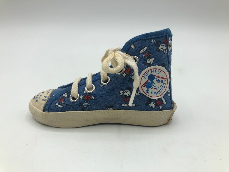 May include: Blue canvas high-top trainers with a white lace-up fastening and a Mickey Mouse and Friends logo patch. The trainers have a white rubber sole.