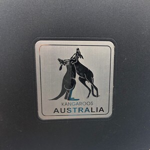 May include: A silver metal sticker with two kangaroos facing each other. The sticker says "Kangaroos Australia".