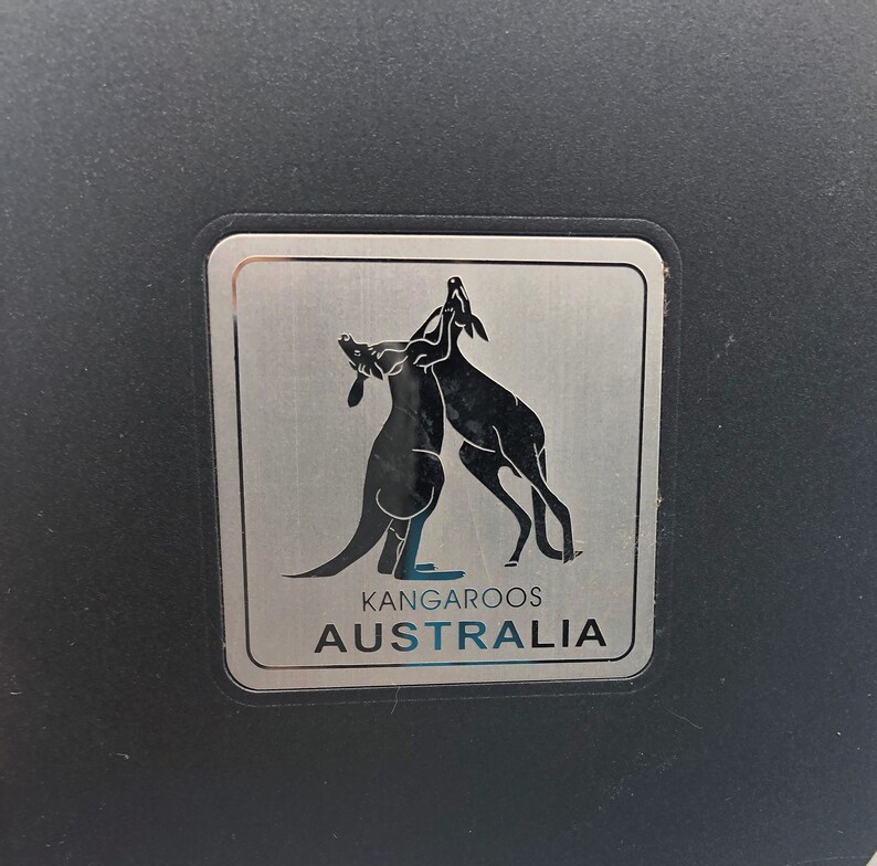 May include: A silver metal sticker with two kangaroos facing each other. The sticker says "Kangaroos Australia".