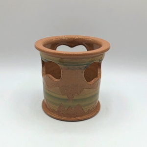 May include: A brown ceramic pot with a decorative design of green and yellow stripes. The pot has three cut-out heart shapes around the middle.