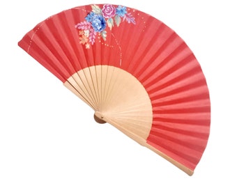 May include: A red folding fan with a floral design painted on the front. The fan is made of paper and has a wooden handle.