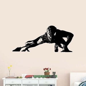 Könnte beinhalten: Schwarze und weiße Silhouette Wandaufkleber eines Superhelden in einer hockenden Pose. Der Superheld trägt eine Maske und einen Anzug mit einem Spinnennetz-Design.