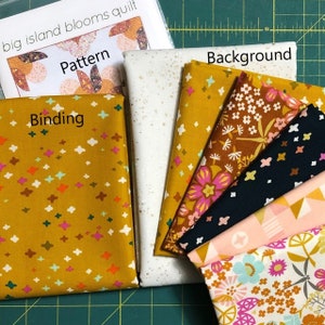 May include: A set of fabric squares for quilting, including a white background fabric with gold flecks, a yellow fabric with white and pink stars, a dark blue fabric with white stars, a pink fabric with geometric shapes, a white fabric with floral patterns, and a brown fabric with floral patterns. The fabrics are labelled "Binding", "Background", and "Pattern".