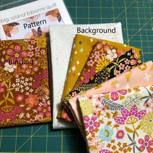 Puede incluir: Un kit de acolchado con piezas de tela en varios patrones florales, incluyendo un fondo blanco con purpurina dorada, una tela amarilla con estrellas blancas, una tela marrón con flores rosas y amarillas, una tela negra con flores rosas y amarillas, una tela rosa con flores amarillas y blancas, y una tela amarilla con flores rosas y blancas. El kit también incluye una hoja de patrón con el texto "big island blooms quilt" y "Pattern".