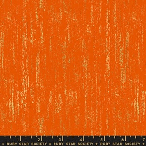 Op de afbeelding: Oranje stof met een gouden metallic textuurpatroon. De stof heeft een subtiel verticaal streepjespatroon. De stof is gemarkeerd met een liniaal en de tekst "RUBY STAR SOCIETY".