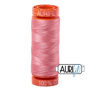 Op de afbeelding: Een spoel Aurifil 100% katoenen draad in een zachte roze tint. De spoel heeft oranje doppen met het Aurifil-logo en tekst. De draad is strak opgerold, wat de textuur en kleur laat zien. Ideaal voor naai- en quiltprojecten.