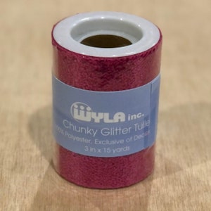 May include: A roll of pink chunky glitter tulle, 3 inches wide and 15 yards long. The label reads "iwLA inc. Chunky Glitter Tulle 100% Polyester, Exclusive of Decor 3 in x 15 yards".