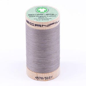 May include: A spool of gray Scanfil 100% organic cotton thread. The spool has a wooden base and top with the brand name printed on it. The label indicates the thread is made in the Netherlands and is 457 meters or 500 yards.