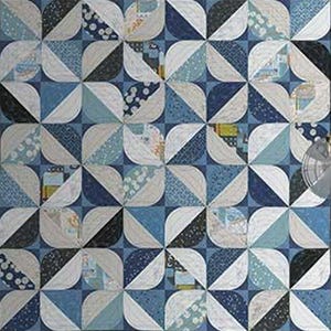 May include: A handmade quilt with a geometric pattern. The quilt features a repeating design of rounded squares in shades of blue, white, and black. The design incorporates various patterned fabrics, creating a visually interesting and textured surface.